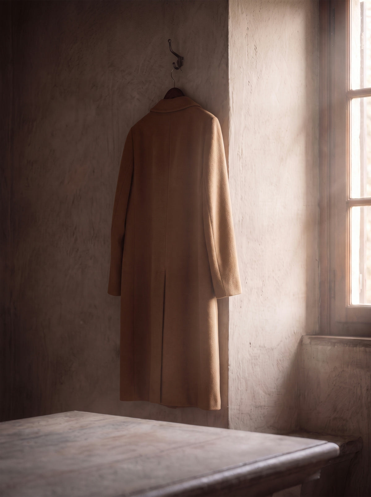 Abrigo largo color camel colgado junto a una ventana con luz suave.